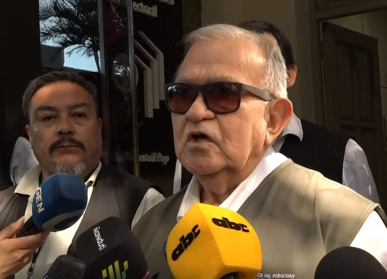 Jorge Bogarín González, con gafas de sol y casaca clara, habla a los medios rodeado de un ambiente urbano.