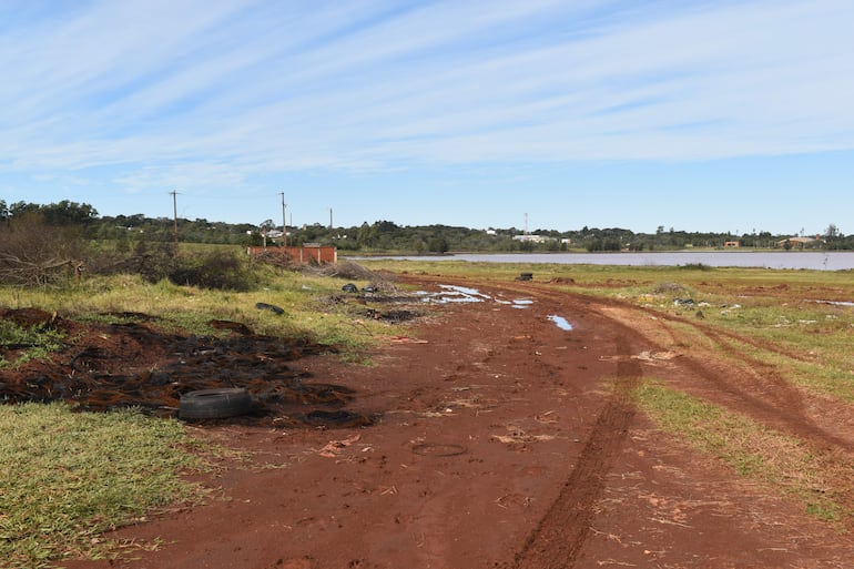 Terreno rural en Encarnación con tierra roja, restos de flora y escombros, y un cuerpo de agua al fondo.