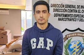 Hombre esposado, vestido con sudadera 'GAP', en oficina de policía con cartel que indica unidad contra el narcotráfico.