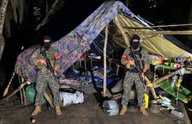 Dos hombres con uniformes de camuflaje y pasamontañas sostienen fusiles frente a un refugio improvisado.