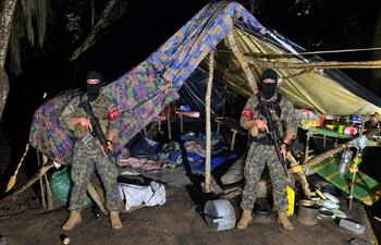 Dos hombres con uniformes de camuflaje y pasamontañas sostienen fusiles frente a un refugio improvisado.