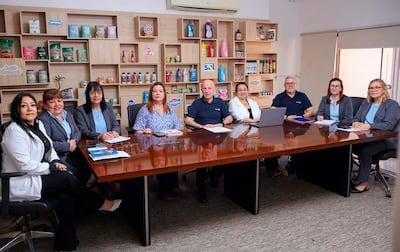 Ocho personas sentadas: mujeres con chaquetas y blusas, hombres con camisetas, en una mesa con documentos y productos embasados.