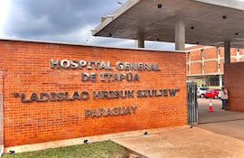 Fachada de ladrillo del Hospital General de Itapúa, con vehículos estacionados y personas en la entrada en un día nublado.