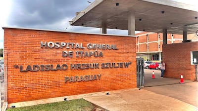 Fachada de ladrillo del Hospital General de Itapúa, con vehículos estacionados y personas en la entrada en un día nublado.