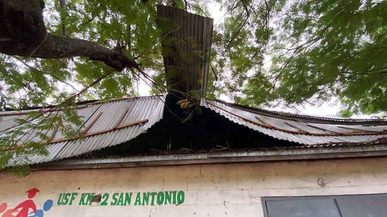 Estructura de salud familiar con techo de chapa dañado, rodeada de ramaje y una pared blanca con el texto 'USF KM 2 SAN ANTONIO'.