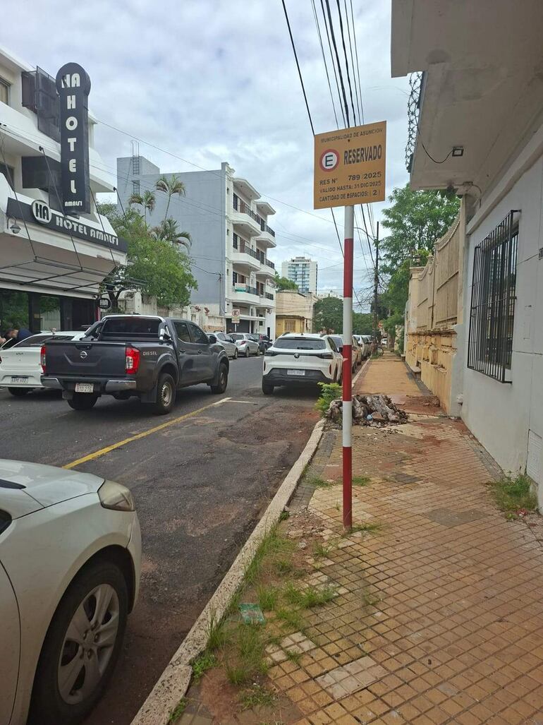 Cartel de estacionamiento reservado en área urbana con vehículos estacionados y el Hotel Amalfi al fondo.