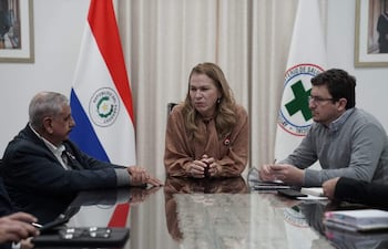 María Teresa Barán habla en reunión, acompañada por Saúl Recalde e Isaías Ricardo Fretes, en ambiente formal con banderas de Paraguay y el Ministerio de Salud.