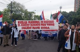 Grupo de médicos enérgicos, con banderas paraguayas, sosteniendo un gran cartel sobre salarios dignos en un ambiente urbano.