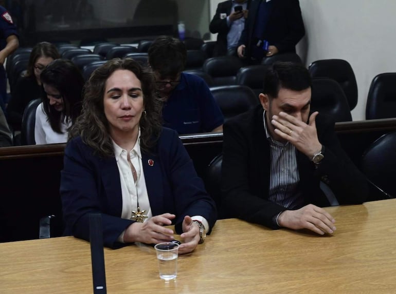 Alba Zaracho con blusa blanca y saco oscuro reflexiona, mientras Hernán Rivas, con camisa de rayas y saco negro, muestra expresión tensa.