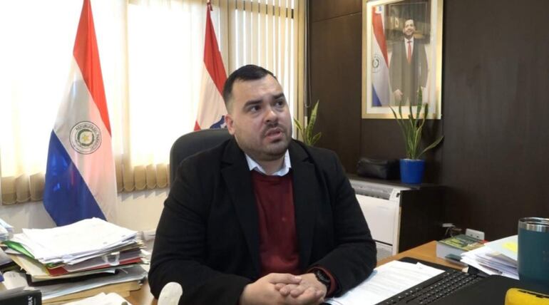 Raúl Luis Latorre Martínez, con saco oscuro y suéter rojo, habla en su oficina con banderas de Paraguay de fondo.