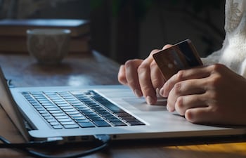 Una persona realiza compras en línea en su computadora laptop con una tarjeta de crédito en la mano.