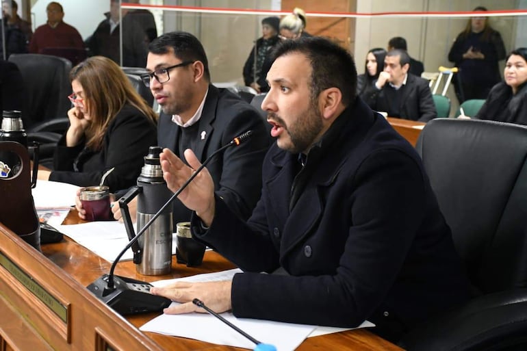 Cesar Escobar Ceres gesticula mientras habla, rodeado de asistentes que lo escuchan atentamente en un entorno formal.