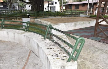 Barandas verdes en mal estado en un espacio recreativo vacío, con superficies de concreto y área de arena.
