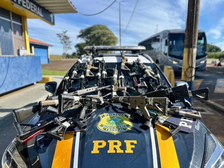 Vehículo patrullero de la Policía Federal con varias armas de fuego sobre su capó en un ambiente exterior.