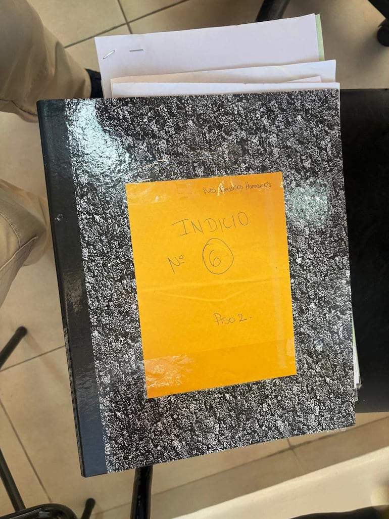 Cuaderno negro con etiqueta amarilla que indica 'INDICIO N° 6' en una superficie interior de oficina.