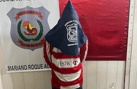 Britez Leguizamon de pie en comisaría, vestido con camiseta de rayas rojas y blancas, con gorro, frente a cartel de Policía Nacional.