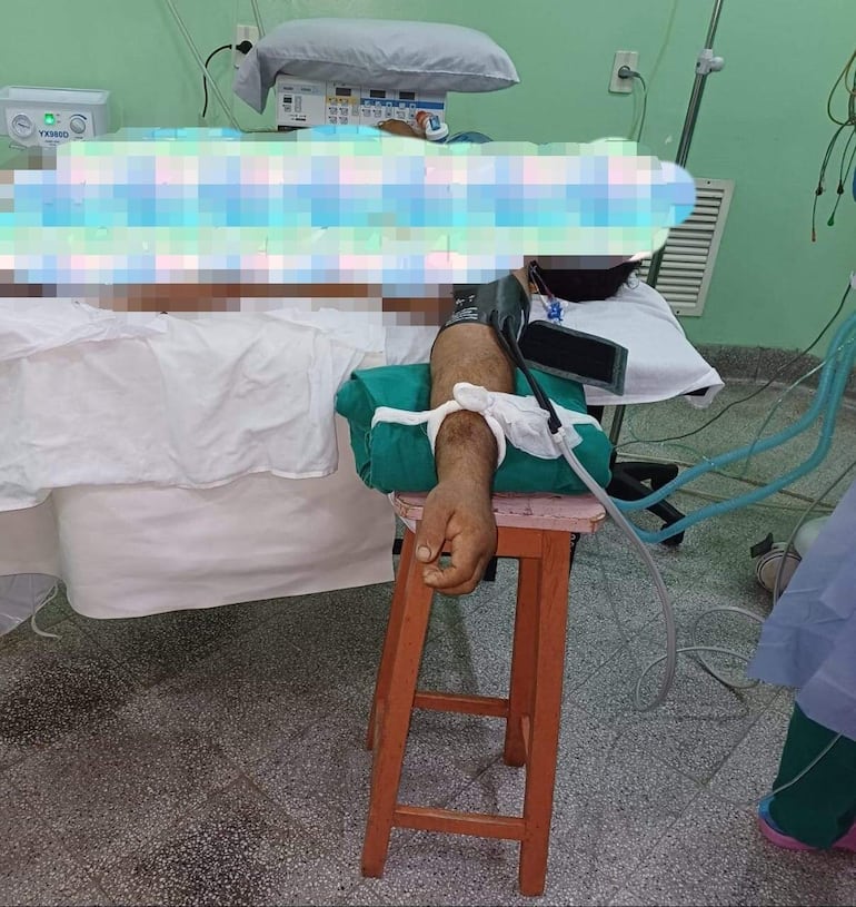 Una butaca de madera hace de soporte para el brazo de un paciente que acaba de salir de cirugía y debe "recuperarse" en una simple camilla de hospital.