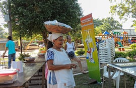 Mujer mayor sonriente con canasta en la cabeza, rodeada de otras personas en un ambiente festivo y comunitario.