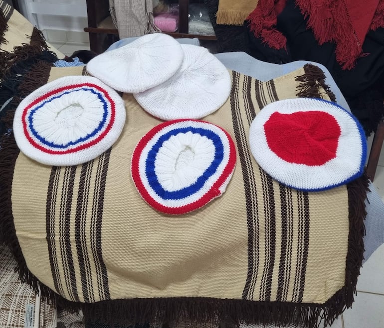Sombreros de lana en colores blanco, rojo y azul exhibidos en una superficie textil beige en un taller.