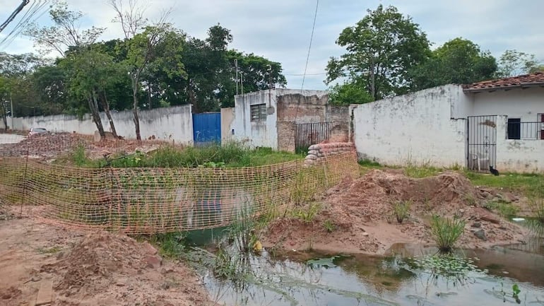 Paisaje urbano en construcción con charca de agua y materiales de obra, sin personas presentes.