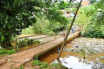 Persona a la derecha del puente, inspeccionando el área inundada con vegetación densa y basura flotante en un entorno urbano.