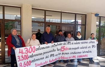 Seis personas sostienen una pancarta en protesta, con expresiones serias en un ambiente urbano.