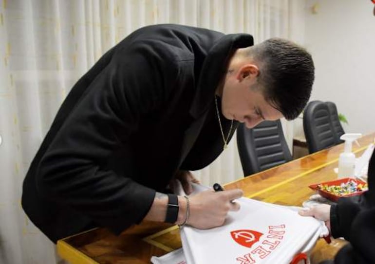 Hombre joven con chaqueta negra firma camiseta blanca con 'INTER' en rojo, en ambiente interior sobrio y bien iluminado.