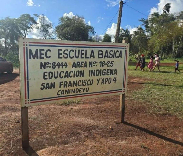 Cartel de la escuela con la junta de personas caminando y un coche estacionado en un entorno rural.