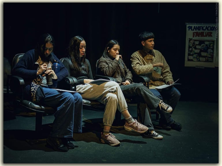 Cuatro personas sentadas, una mujer con abrigo oscuro, otra pensativa, una más concentrada en un papel, y un hombre gesticulando en chaqueta clara.