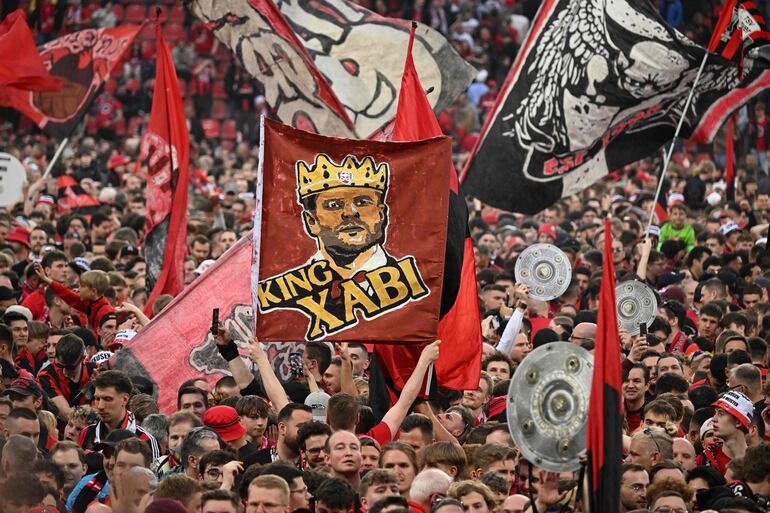TOPSHOT - Leverkusen fans celebrate on the pitch with a banner of "King Xabi" (Bayer Leverkusen's Spanish head coach Xabi Alonso) after the German first division Bundesliga football match Bayer 04 Leverkusen v Werder Bremen in Leverkusen, western Germany, on April 14, 2024. Bayer Leverkusen were crowned 2023-24 Bundesliga champions for the first time on April 14, 2024.  (Photo by INA FASSBENDER / AFP) / DFL REGULATIONS PROHIBIT ANY USE OF PHOTOGRAPHS AS IMAGE SEQUENCES AND/OR QUASI-VIDEO