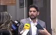 Raúl Benítez en traje gris claro, rodeado de reporteros con micrófonos, en la Comisión de Presupuesto con inscripción detrás.