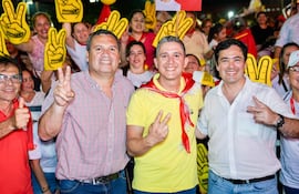 Derlis Maidana con camisa de cuadros, Hans Kemper en camiseta amarilla y bufanda roja, Rodrigo Gamarra en camisa blanca, sonríen y hacen gestos de paz.