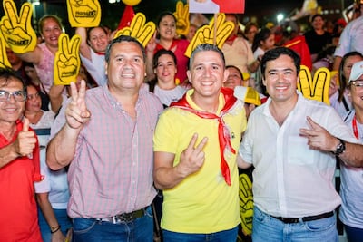 Derlis Maidana con camisa de cuadros, Hans Kemper en camiseta amarilla y bufanda roja, Rodrigo Gamarra en camisa blanca, sonríen y hacen gestos de paz.
