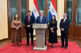 Óscar Lovera en traje claro, flanqueado por Teodora Recalde en vestido marrón y Andrea Picaso en vestido negro, todos en ambiente formal.