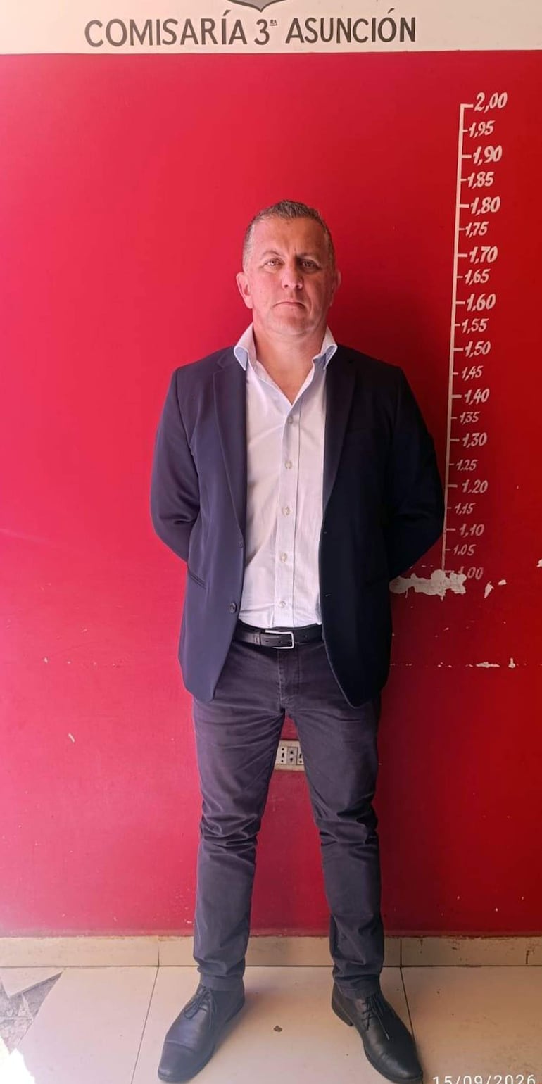 Cristian Porfirio Amarilla Cabaña, de pie y con traje oscuro, frente a la pared roja de la comisaría.