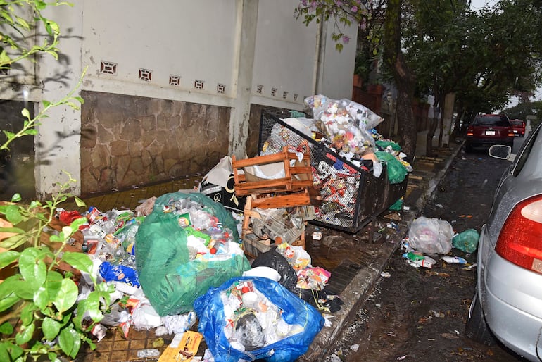 Basura acumulada en calle húmeda, con contenedor volcado y bolsas plásticas alrededor en Teodoro S Mongelos y 22 de Setiembre