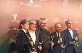 Cinco personas, cuatro hombres y una mujer, sosteniendo trofeos en un evento de gala, con expresiones de felicidad en un ambiente decorado.