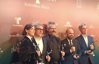 Cinco personas, cuatro hombres y una mujer, sosteniendo trofeos en un evento de gala, con expresiones de felicidad en un ambiente decorado.