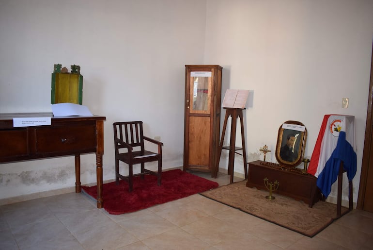 Espacio interior con escritorio de madera, silla, bandera paraguaya y detalles decorativos en un ambiente de exhibición.