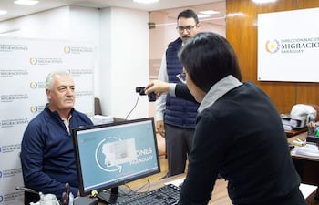 Gustavo Alfaro sentado frente a una computadora mientras otros dos observan la gestión en oficina formal.