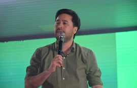 Eduardo Desjesus, con camisa verde, sostiene un micrófono mientras habla en un auditorio iluminado.