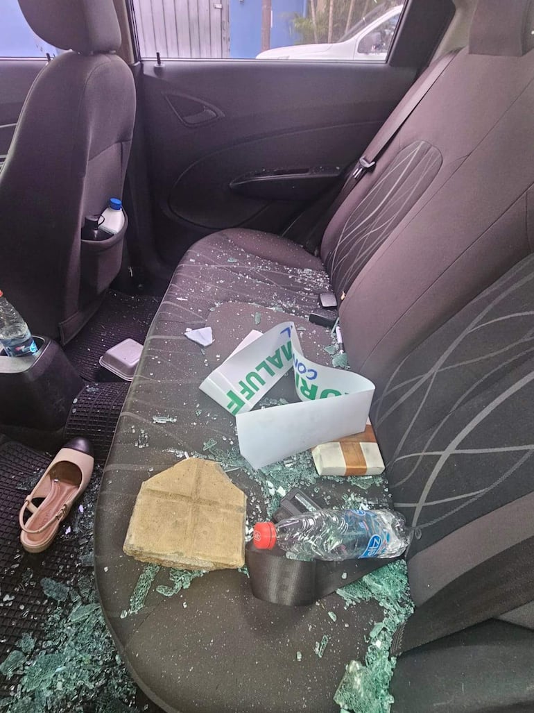 Interior de un automóvil dañado con vidrio roto, objetos desordenados y una zapatilla de mujer.
