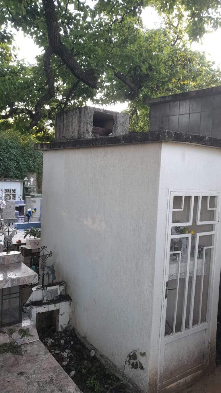 Mausoleo blanco cubierto de maleza en un cementerio tranquilo y descuidado, sin personas visibles.