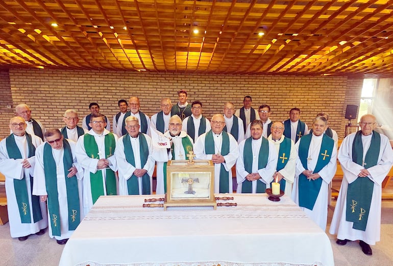 Veinte clérigos de pie, vestidos con estolas verdes en una capilla, junto a un altar con un candelabro encendido.