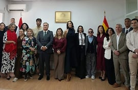 Belén Vierci en abrigo rojo, rodeada de personas felices en un ambiente formal, con bandera paraguaya de fondo.