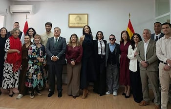 Belén Vierci en abrigo rojo, rodeada de personas felices en un ambiente formal, con bandera paraguaya de fondo.