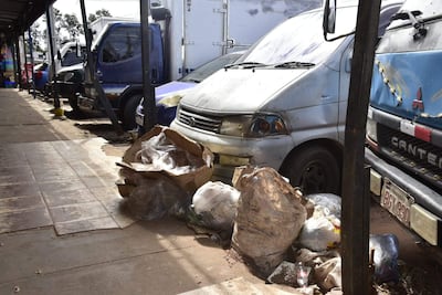 Acumulación de basura en acera del Mercado de Abasto, con vehículos estacionados y un ambiente descuidado.