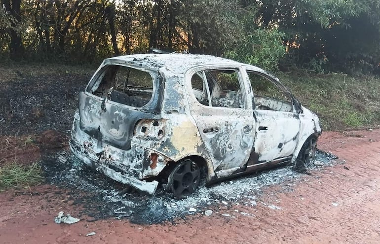 Automóvil completamente quemado en una calle rural, rodeado de vegetación y cubierto de cenizas.