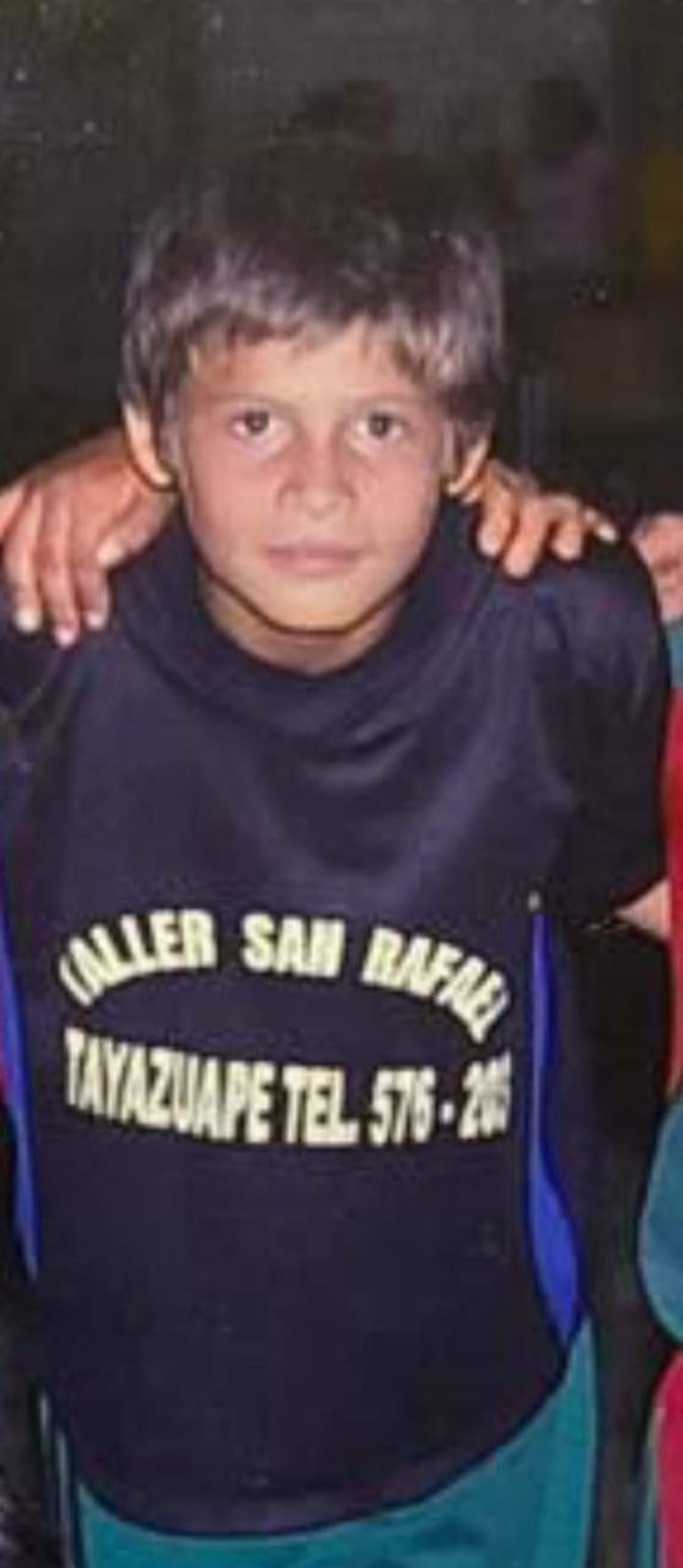 Orlando Gill con camiseta oscura y amarilla, rodeado de niños en la escuela Tayazuape, posando con expresiones serias.