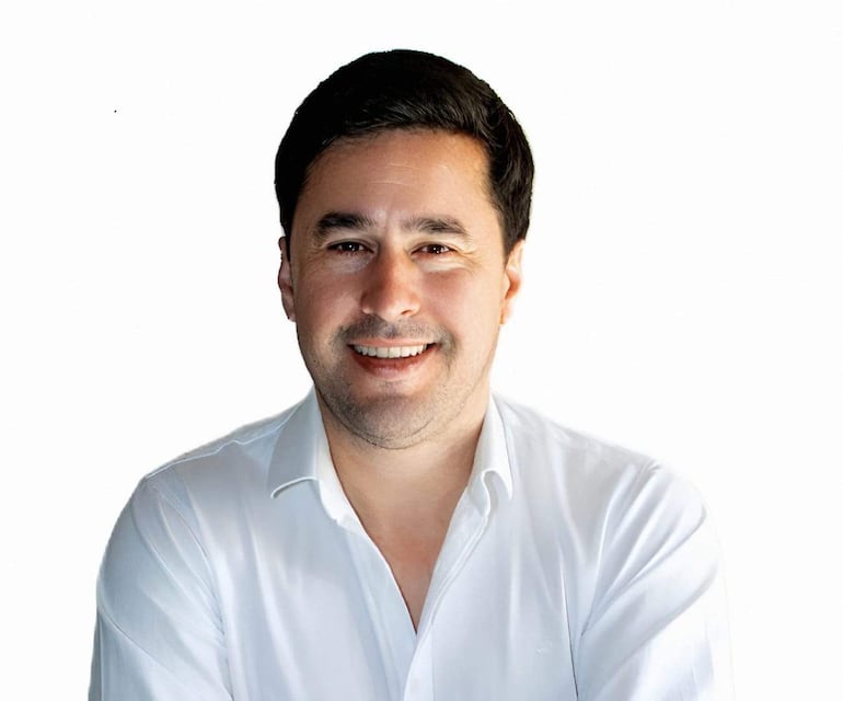 Eduardo Dejesús sonriente con camisa blanca, mirando a la cámara en un fondo blanco.